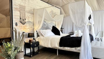 Ein Zeltraum mit Bett, Nachttisch, Lampe und einer Wanddekoration.