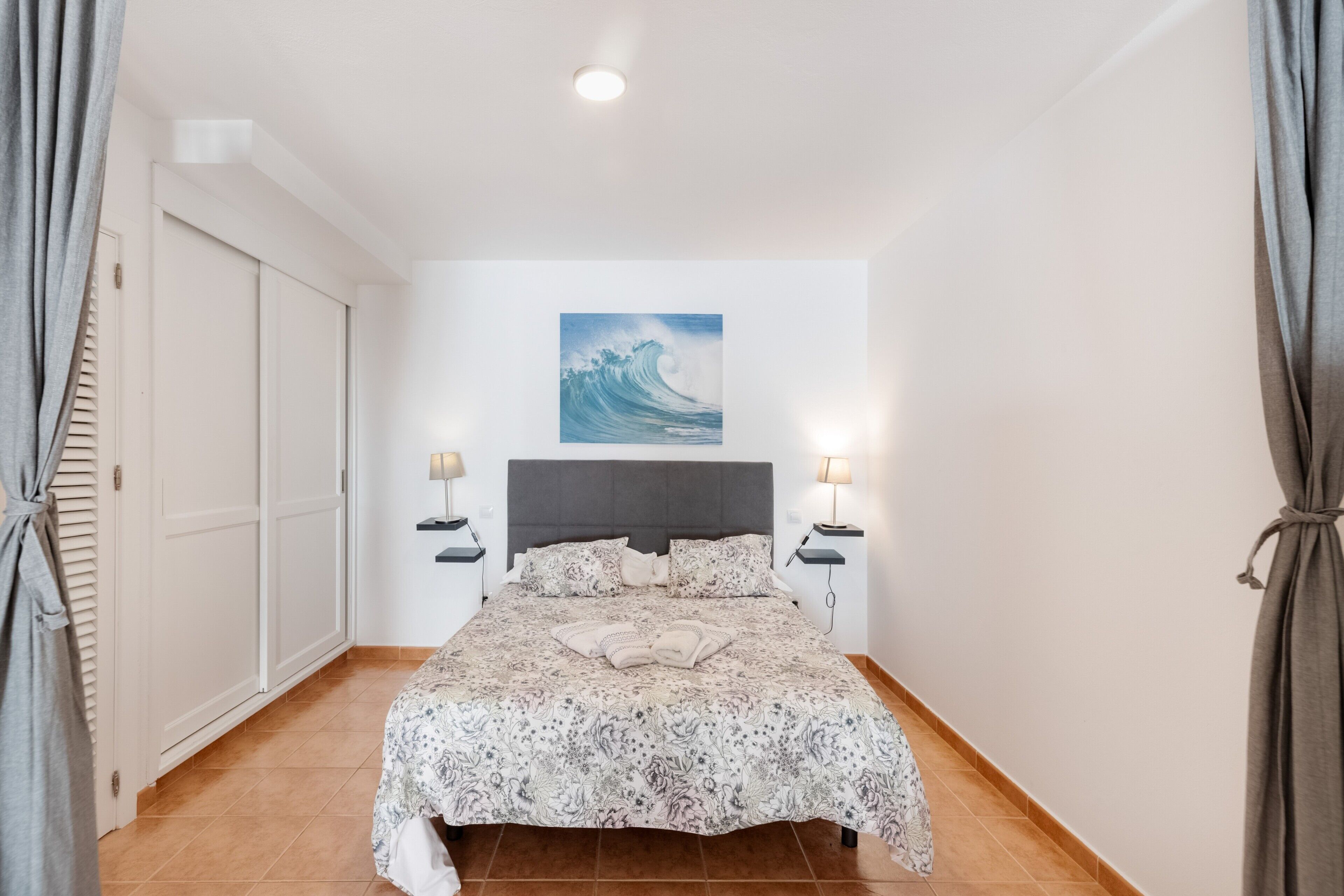 Une chambre à coucher avec un lit, un tableau, deux tables de chevet et une porte.
