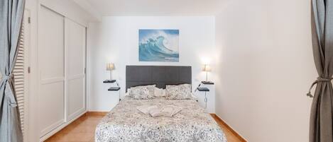 Une chambre à coucher avec un lit, un tableau, deux tables de chevet et une porte.
