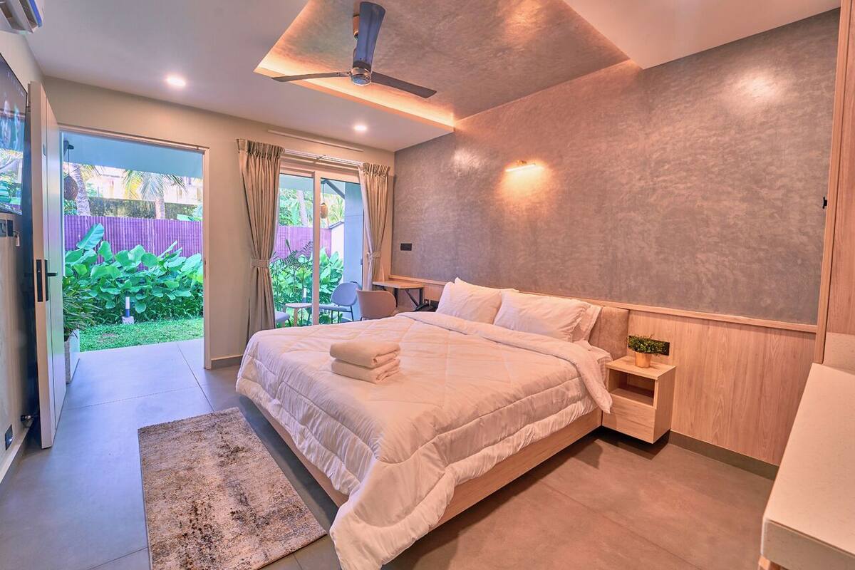 Un dormitorio moderno con una cama grande, un ventilador de techo y vistas a un jardín a través de una puerta corredera.