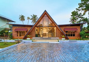 A modern building with a triangular glass facade, a wooden exterior, and a paved entrance area. - Kayal Cove Resort by VOYE HOMES (Alappuzha)