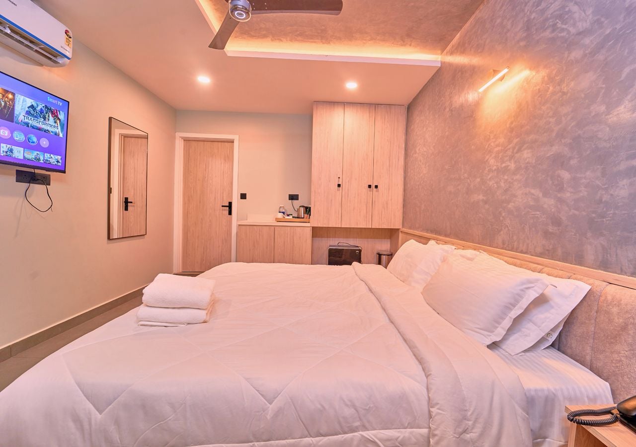 A hotel room with a bed, a TV, a wardrobe, and a desk with a chair.