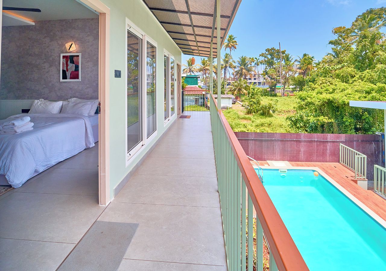 A hotel room with a balcony, a bed, a small pool, and a view of palm trees and greenery.
