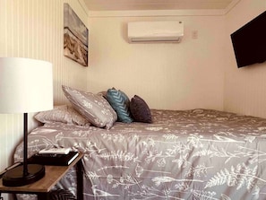 Une chambre à coucher avec un lit, des oreillers, une lampe, une télécommande et un climatiseur.