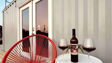 Une terrasse avec une chaise rouge, une table avec deux verres à vin et une bouteille, et une pancarte indiquant : « Bienvenue dans notre maison au bord du lac ».