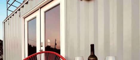 A deck with a red chair, a table with two wine glasses and a bottle, and a 'Welcome to our Lakehouse' sign.