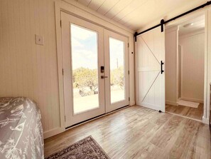 Une chambre avec un lit, une porte coulissante donnant sur un balcon et un plancher en bois.