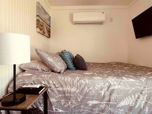 Une chambre à coucher avec un lit, des oreillers, une lampe, une télécommande et un climatiseur.