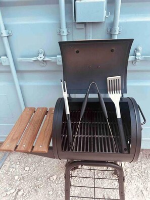 A portable grill with a lid open, two barbecue utensils, and a wooden tray. - Tiny Container For A Glamping Getaway with Canyon Lake Views Close to Austin, Texas (Canyon Lake)