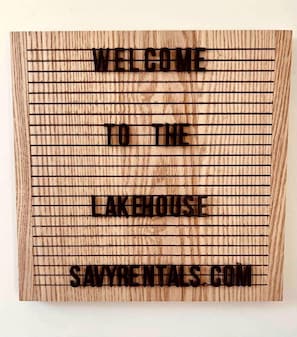 Een houten bord met de tekst 'WELCOME TO THE LAKEHOUSE SAVYRENTALS.COM'.
