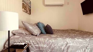 Quarto com cama, almofadas, luminária, controle remoto e ar condicionado.