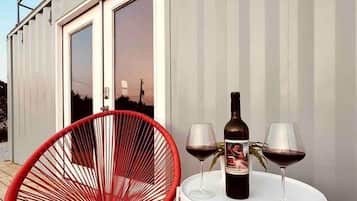 Une terrasse avec une chaise rouge, une table avec deux verres à vin et une bouteille, et une pancarte indiquant : « Bienvenue dans notre maison au bord du lac ».