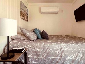 Een slaapkamer met een bed, kussens, een lamp, een afstandsbediening en een airconditioner.