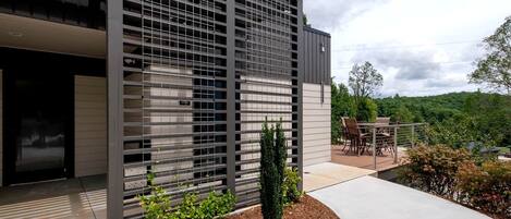 Un bâtiment moderne doté d’une façade métallique, d’un patio aménagé avec du mobilier d’extérieur et offrant une vue sur un paysage verdoyant.