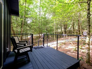 Une terrasse en bois avec deux chaises et une rambarde donnant sur une zone boisée.