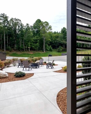 An outdoor patio area with seating and a fire pit, surrounded by a landscaped garden and trees.