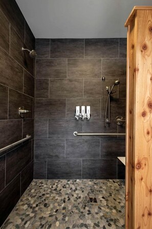A shower with dark tiles, a wooden door, and a pebble-patterned floor.