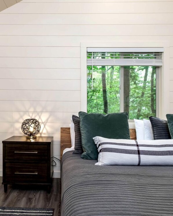 A bedroom with a bed, a nightstand, a lamp, and a window with a view of trees.