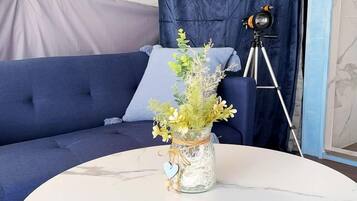 Une table ronde en marbre, sur laquelle se trouve un vase de fleurs, un trépied et un canapé bleu agrémenté d’un rideau, dans une pièce.
