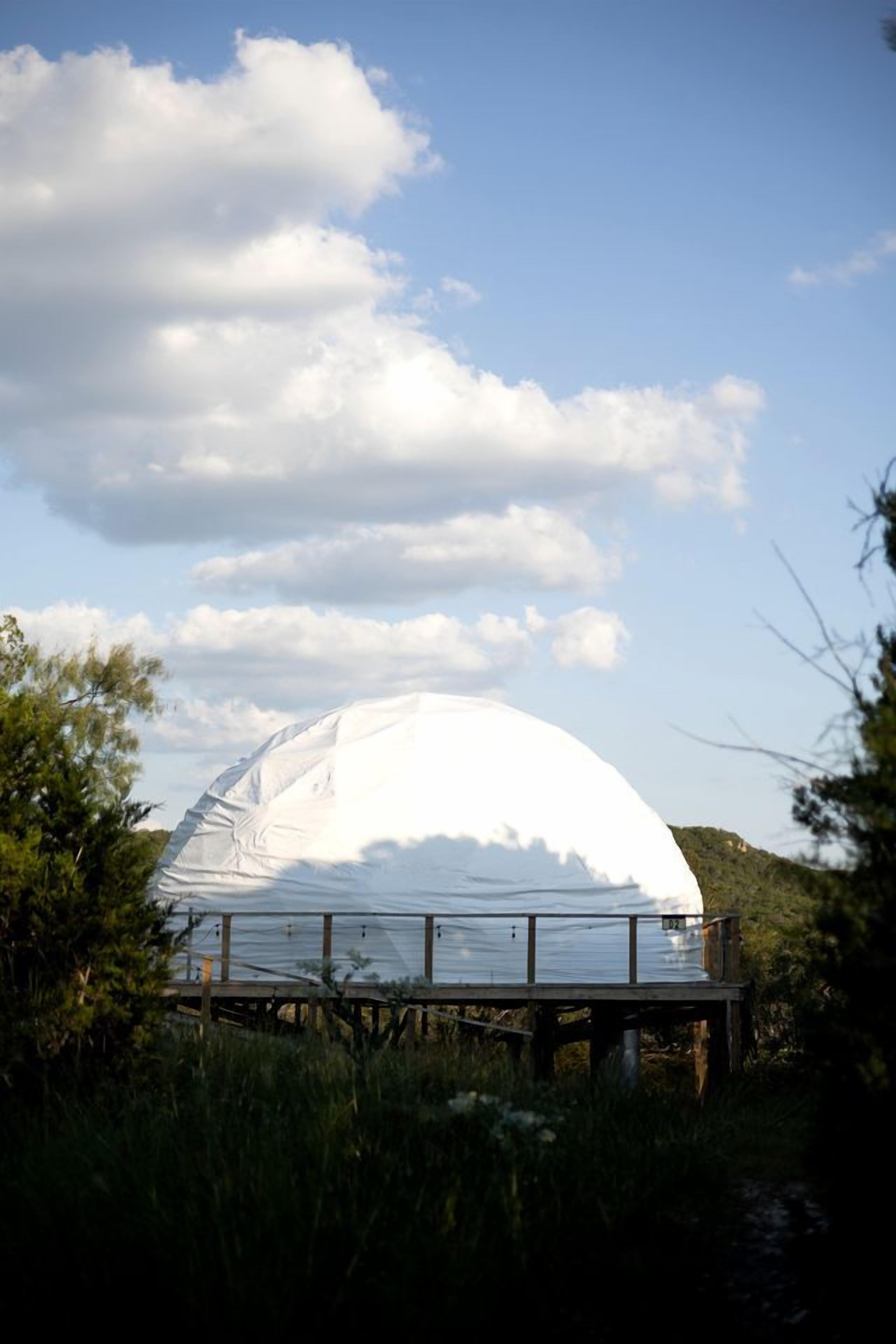 A dome structure with a wooden deck in front, surrounded by vegetation.