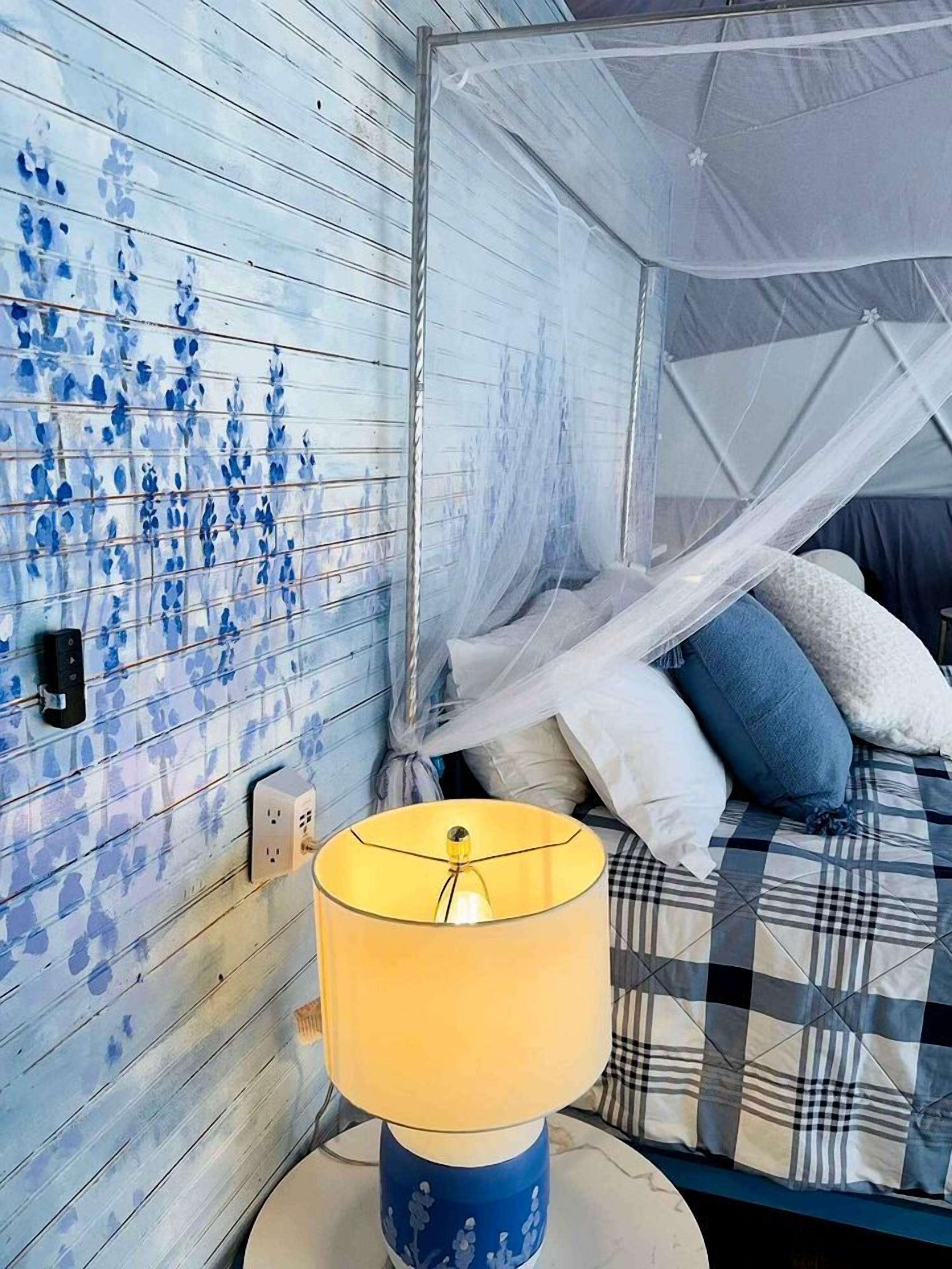 Una habitación con cama, dosel, lámpara y pared con diseños azules.