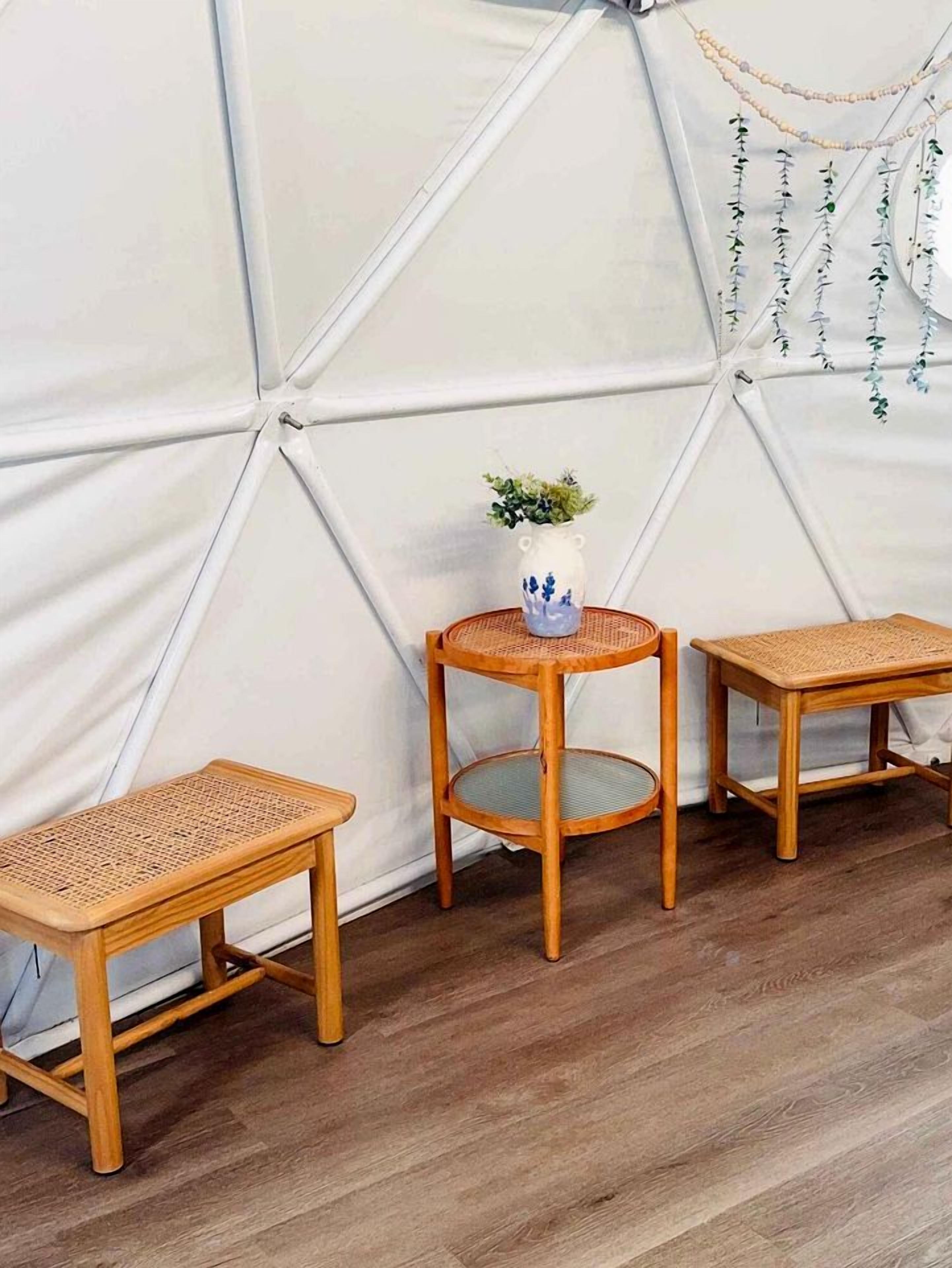 Une pièce dotée d’une structure blanche en forme de tente, de trois tables en bois et d’un vase contenant une plante.