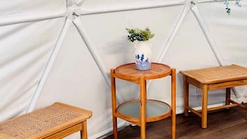 Une pièce dotée d’une structure blanche en forme de tente, de trois tables en bois et d’un vase contenant une plante.