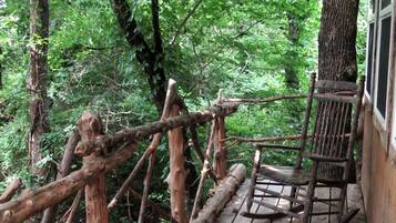A wooden deck with a rocking chair, surrounded by dense forest.