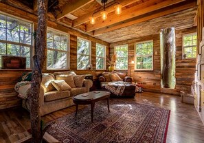A log cabin interior with a sofa, armchairs, a coffee table, and a large rug. - Creekside Tree House with Private Pool in Celeste, Texas, for Memorable Glamping Stays in the South (Celeste)