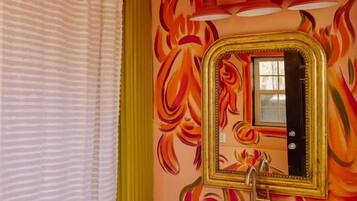 A bathroom with a colorful mural, a white sink, and a gold-framed mirror.