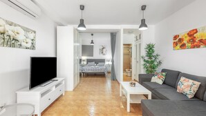 A modern living room with a flat-screen TV, a sofa, a coffee table, and a bed in the background. - Vacation Studio 'Caracola' with Mountain View, Wi-Fi and Air Conditioning (Puerto de Mogán)