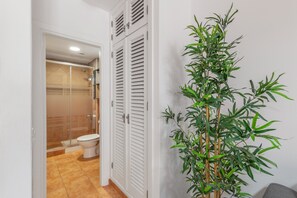 Casa de banho com sanita, chuveiro e uma planta branca.