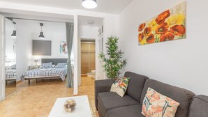 A modern living room with a sofa, a coffee table, a bed with checkered bedding, a plant, and a painting on the wall. - Vacation Studio 'Caracola' with Mountain View, Wi-Fi and Air Conditioning (Puerto de Mogán)