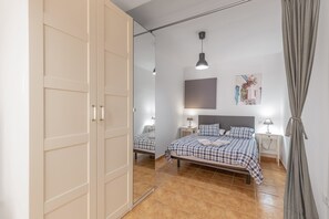 Quarto com cama, mesas de cabeceira, espelho, luminária pendente e uma porta.