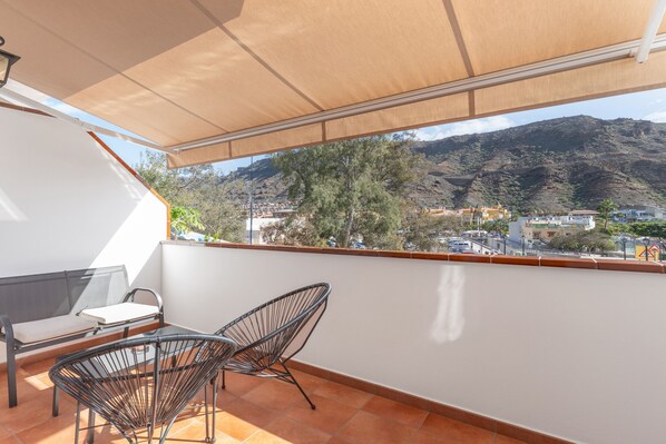 Varanda com vista para uma cidade e montanhas, um sofá e duas cadeiras.