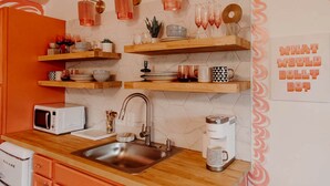Eine Küche mit Mikrowelle, Spüle, Kaffeemaschine und Dekorationen auf Regalen.