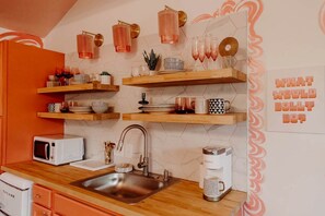 Eine Küche mit Mikrowelle, Spüle, Kaffeemaschine und Dekorationen auf Regalen.