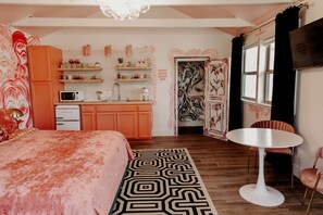 Een slaapkamer met een bed, een kleine kitchenette, een ronde eettafel en een stoel.