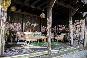 Ein überdachter Außenbereich mit Korbmöbeln, einer Neonreklame und Wandgraffiti.