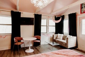Ein Zimmer mit einer Couch, zwei Stühlen, einem Tisch, einer Hängelampe und einem Fernseher.