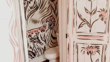 A bathroom with floral wallpaper, a white toilet, and a wooden floor.