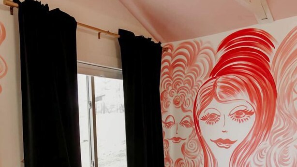 Ein Zimmer mit zwei rosafarbenen Stühlen, einem kleinen Tisch, einem gemusterten Teppich und einer Wandmalerei.