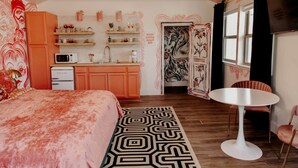 Ein Schlafzimmer mit Bett, einer kleinen Küchenzeile, einem runden Esstisch und einem Stuhl.