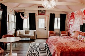 A room with a bed, two chairs, a table, a door, and a window.