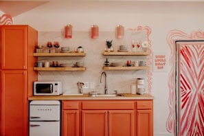A kitchen with orange cabinets, a white refrigerator, wooden shelves with kitchenware, a sink, and a microwave. - Charm in the Mountains: Your Nicest Getaway Awaits at Our One-of-a-Kind Tracy City Cabin (Tracy City)