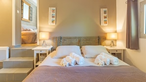 A hotel room with a bed, two bedside tables, a headboard, and a view of another room.