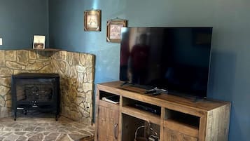 A living room with a stone fireplace, wooden entertainment unit, and an air conditioning unit mounted on the ceiling.