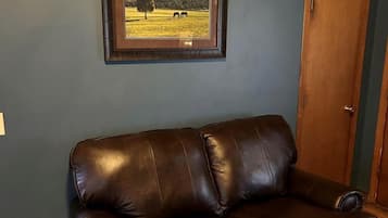 A brown leather sofa against a blue wall with a framed landscape picture above it.