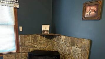 A stone fireplace with a black wood-burning stove, a framed picture on the wall, and a window with blinds.