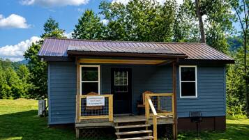 A small, single-story cabin with a porch, a sign indicating it is a campground cottage, and a gravel driveway.